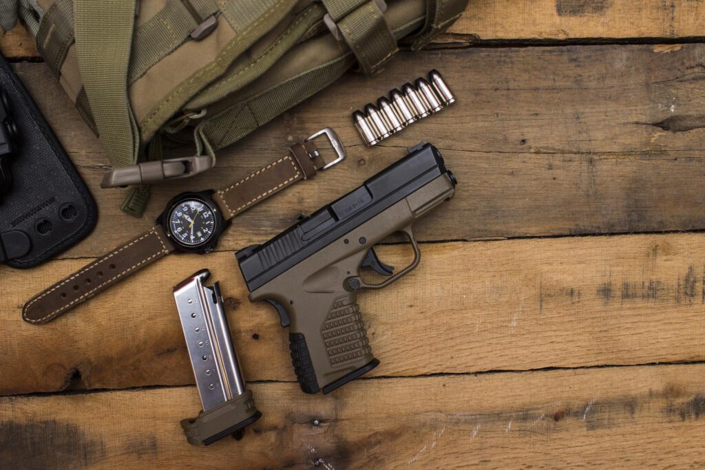 gun range bag on a wooden table, along with handgun, ammo, wristwatch, bullets and magazine